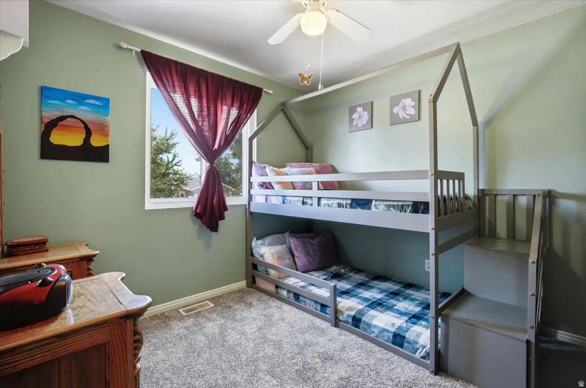 Versatile bedroom featuring a canopy-style bunk bed with built-in storage shelving, soft sage-green walls, and abundant natural light from a large window
