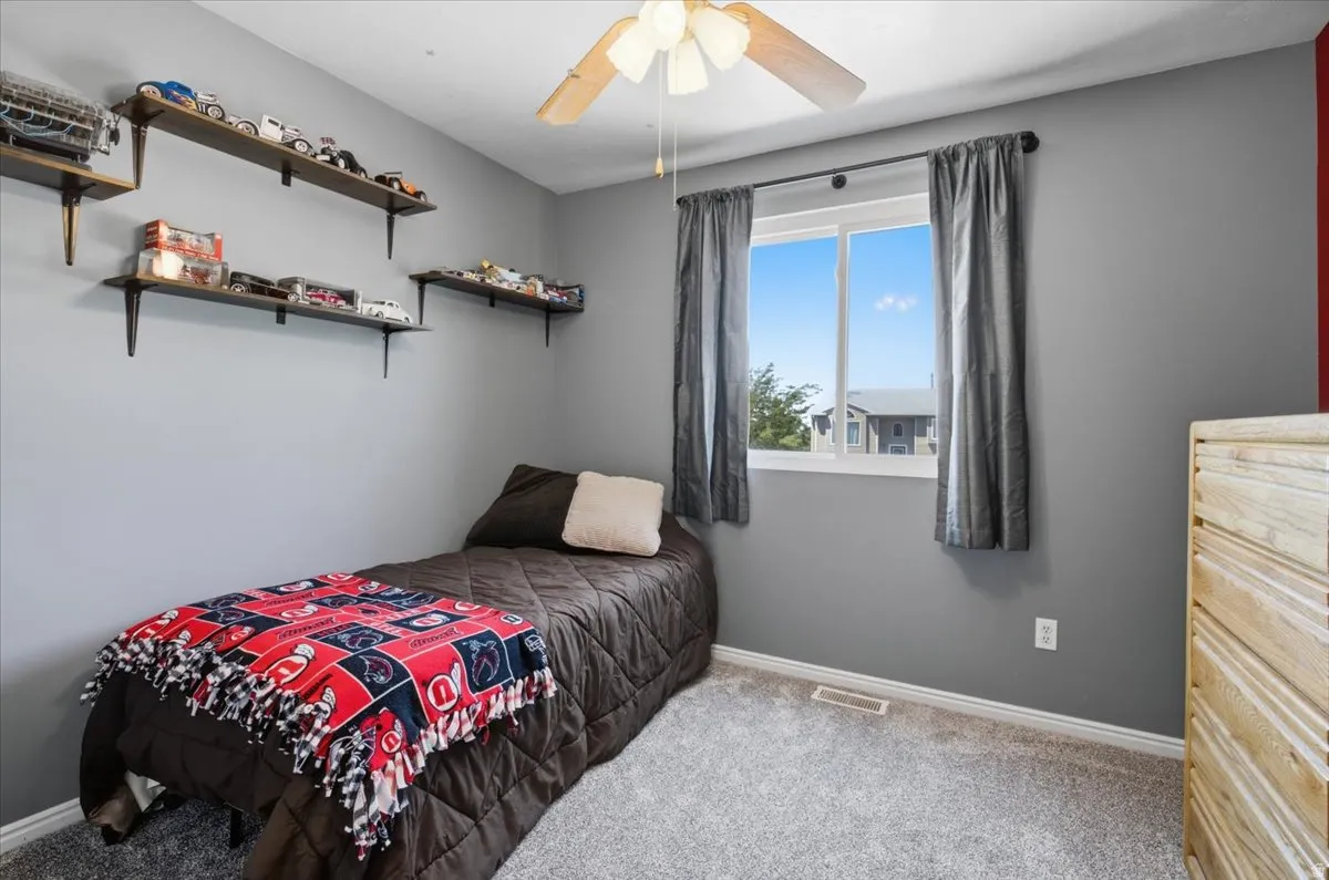 Window-equipped room featuring light gray walls, plush gray carpeting, built-in shelving, a ceiling fan, and white trim