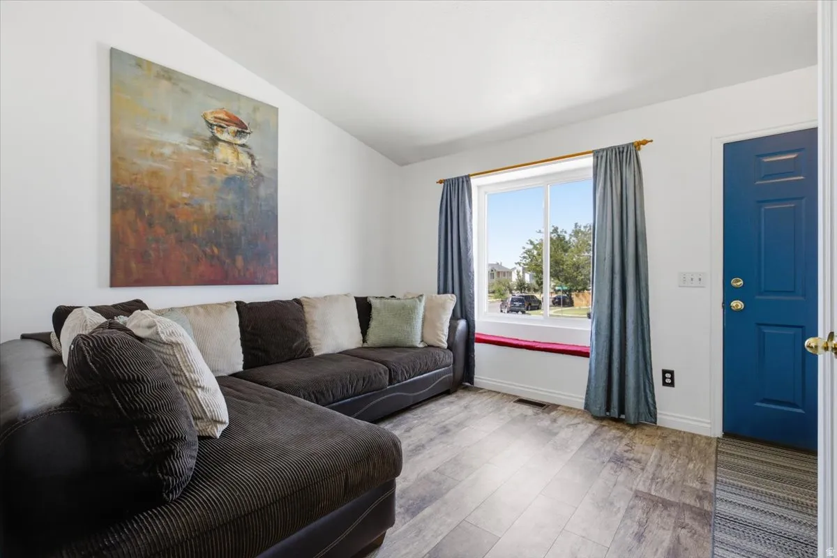 Bright and airy living room featuring a sectional layout with textured upholstery, large picture windows with blue curtains and window seat, wood-finish flooring, and accent artwork