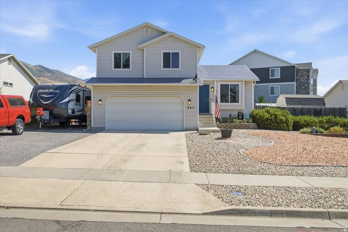 Two-story home featuring a three-car garage with an expansive concrete driveway, neutral exterior siding, and a gabled roofline