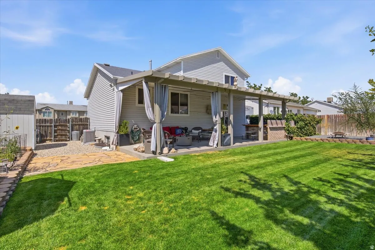 Spacious backyard oasis featuring a manicured lawn with mature landscaping, covered patio with overhead beams, and direct access to the home's rear elevation