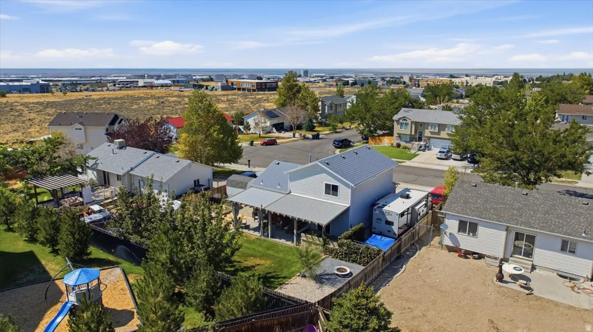 Spacious suburban property featuring a two-story residence with light gray siding and a gray metal roof, complemented by a covered patio area