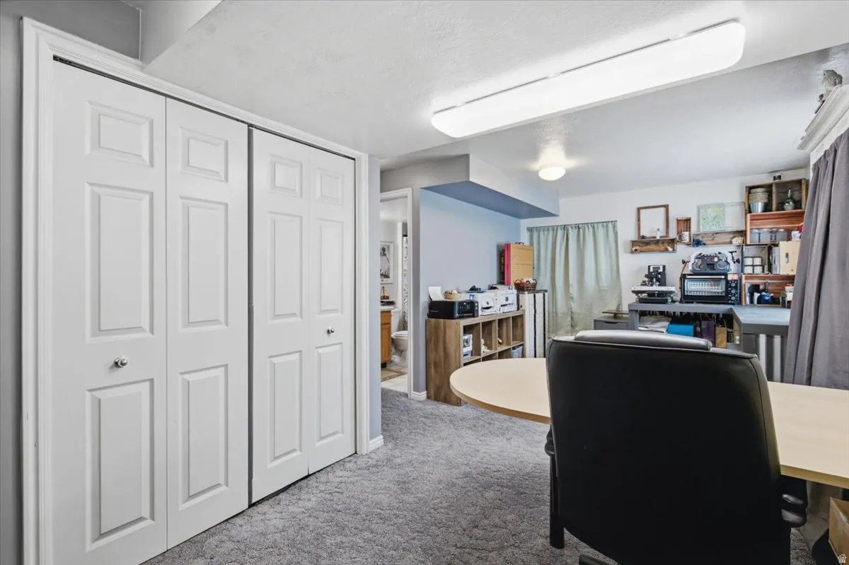 Versatile basement recreation room featuring expansive carpeted flooring, recessed and pendant lighting throughout, built-in shelving and storage cabinetry, a large work surface counter, and direct access to additional finished spaces