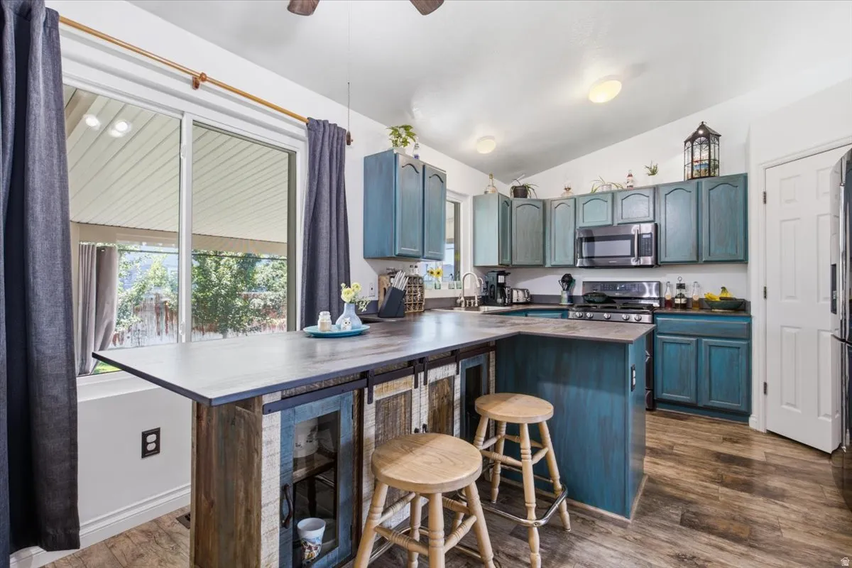 Kitchen featuring teal cabinetry, dark countertops, built-in microwave, gas range, and wood-finish flooring