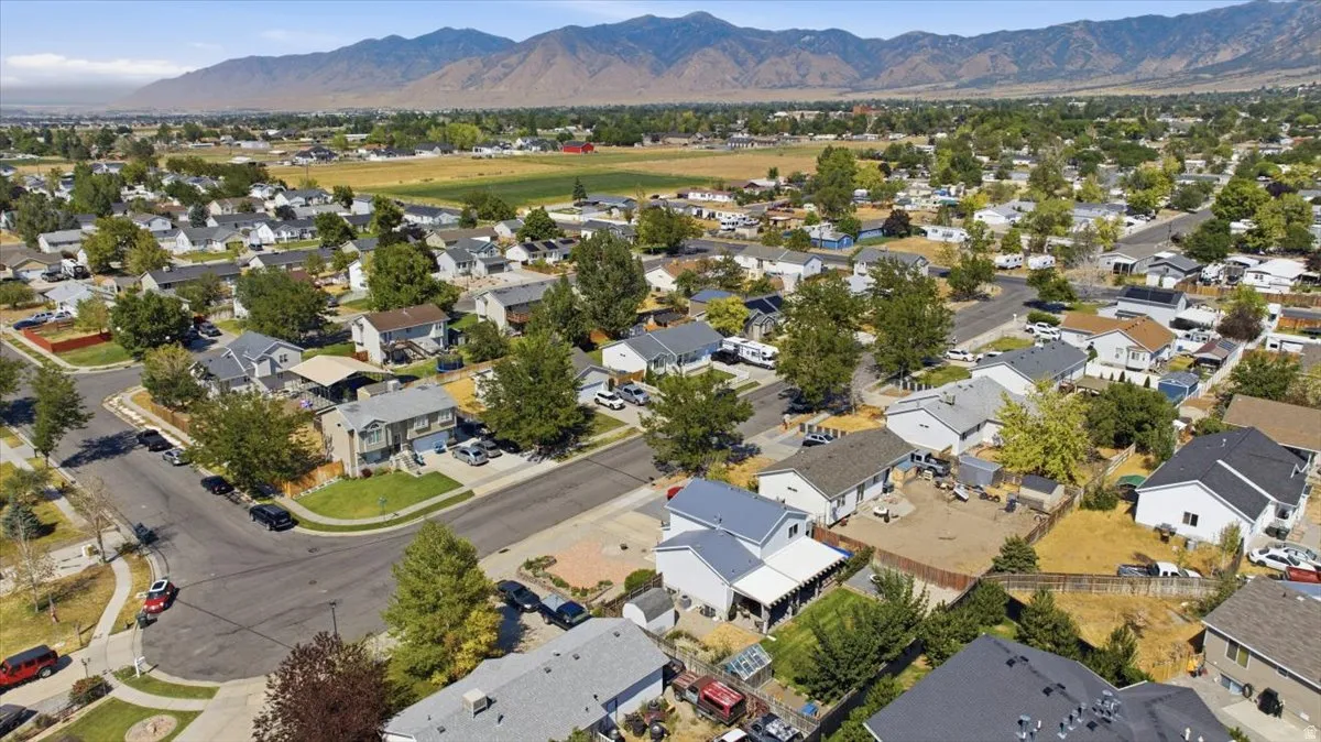 Aerial view showcasing this residential property situated within an established neighborhood featuring mature landscaping, tree-lined streets, and mountain backdrop