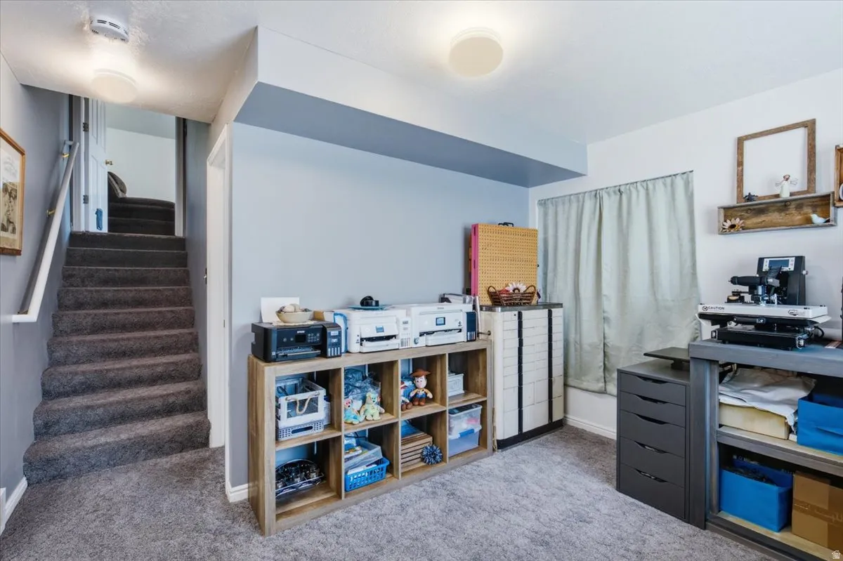 Finished basement recreation room featuring built-in wooden shelving with ample storage cubbies, carpet flooring, recessed ceiling lighting, and a blue accent wall