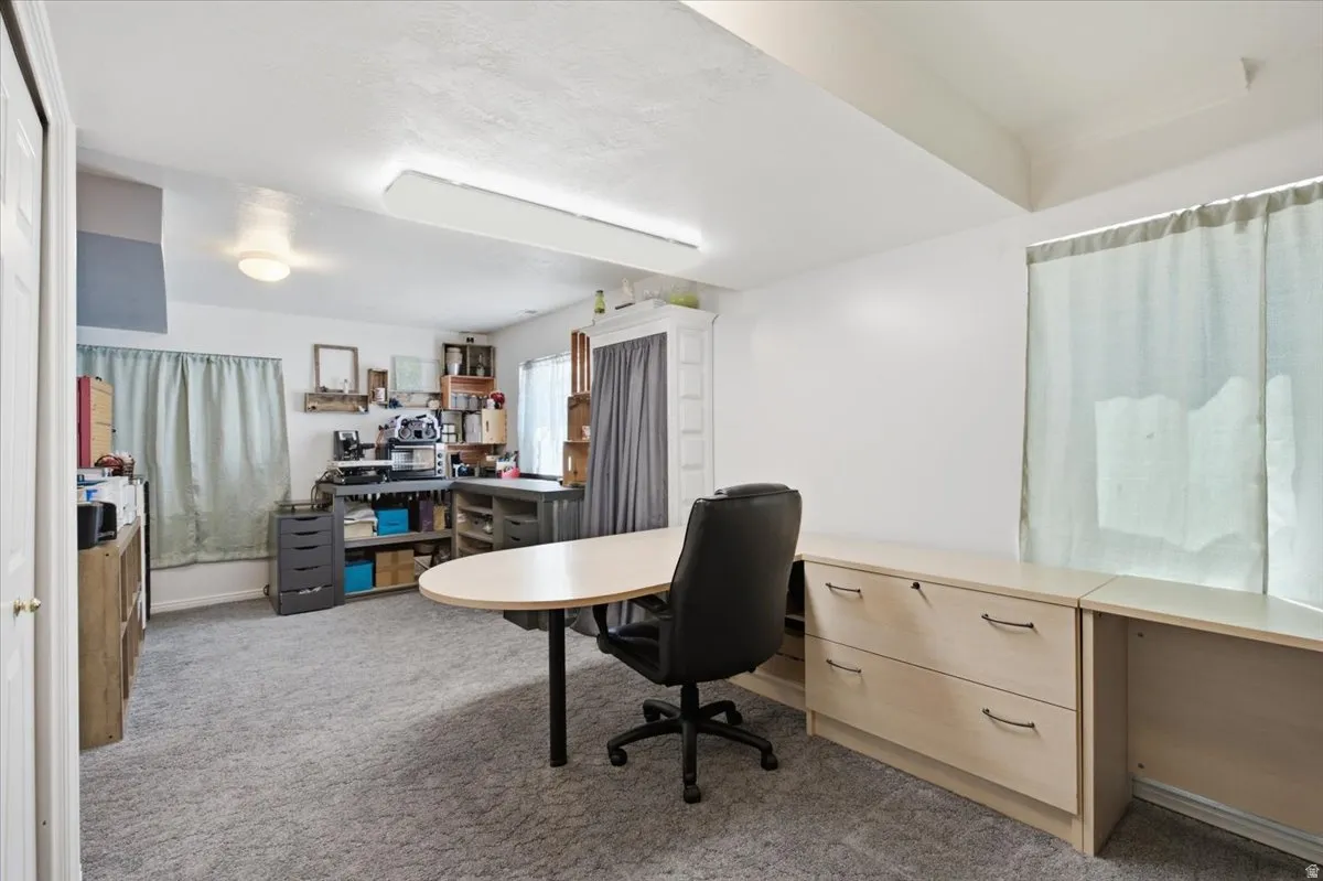 Versatile multi-purpose room featuring expansive carpeted flooring, abundant natural light from large windows, built-in cabinetry with ample storage, a round work table with black task chair, and a comprehensive layout ideal for home office, studio, or cr