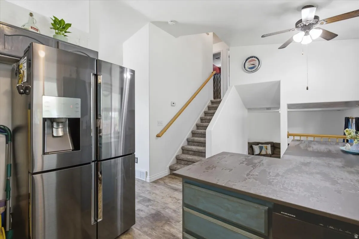 Modern kitchen featuring stainless steel French-door refrigerator with ice and water dispenser, gray quartz countertops, and a teal-finished island with seating