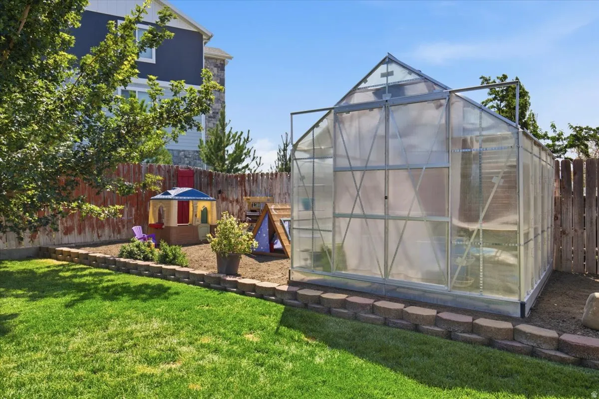 Spacious backyard oasis featuring a mature lawn, established shade trees, and a polycarbonate greenhouse structure with aluminum framing