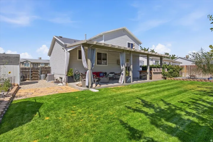 Spacious backyard oasis featuring a manicured lawn with mature landscaping, covered patio with overhead beams, and direct access to the home's rear elevation