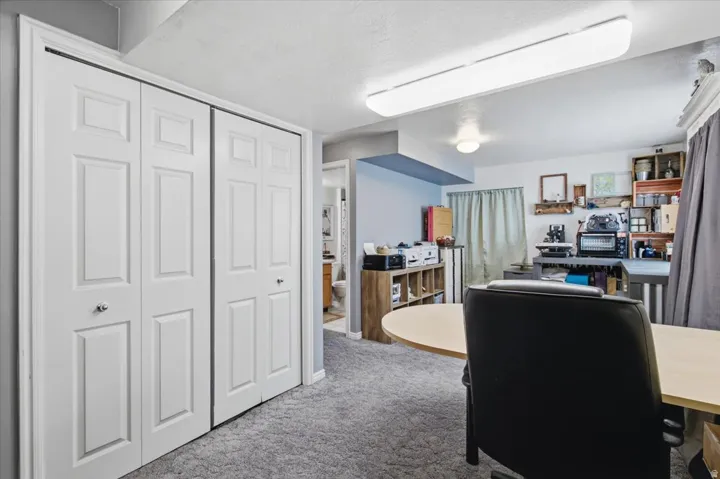 Versatile basement recreation room featuring expansive carpeted flooring, recessed and pendant lighting throughout, built-in shelving and storage cabinetry, a large work surface counter, and direct access to additional finished spaces
