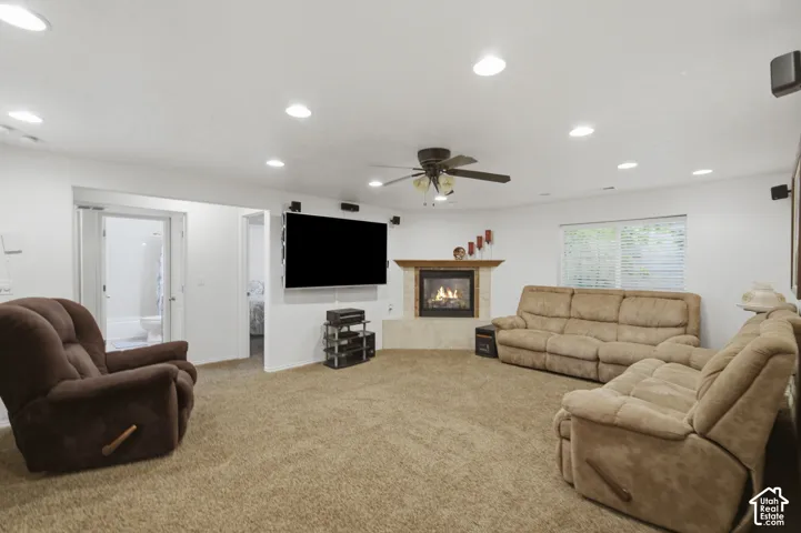 Spacious recreation room featuring recessed ceiling lighting, ceiling fan, and wall-mounted flat-screen television near a fireplace with mantel