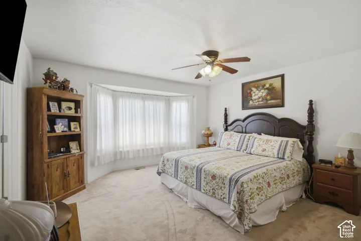 Spacious primary bedroom featuring a bay window, ceiling fan, and carpeted flooring