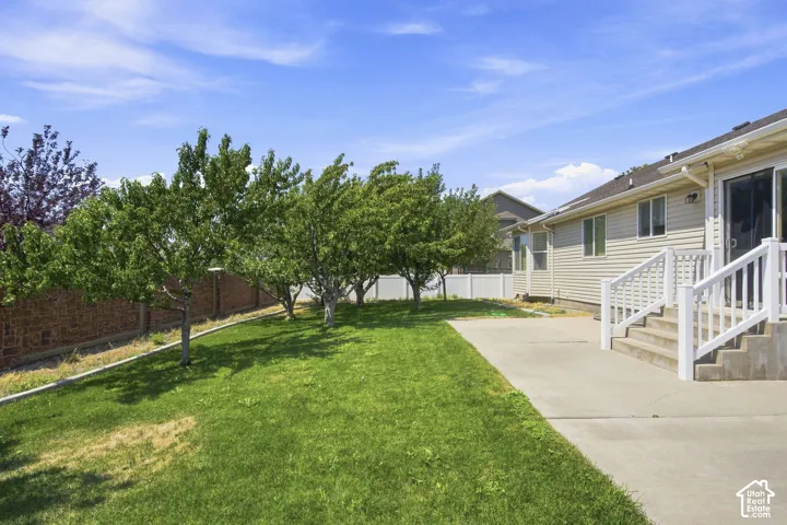 Spacious backyard featuring a large concrete patio, mature trees, a manicured lawn, and a brick privacy wall