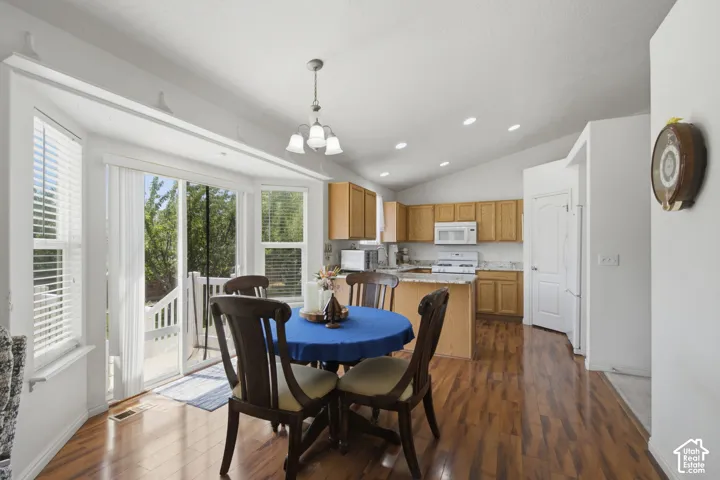 Open-concept kitchen and dining area featuring bamboo flooring throughout, wood cabinetry with white appliances, a round dining table with seating for four, pendant lighting, recessed ceiling lights, and direct access to an outdoor porch