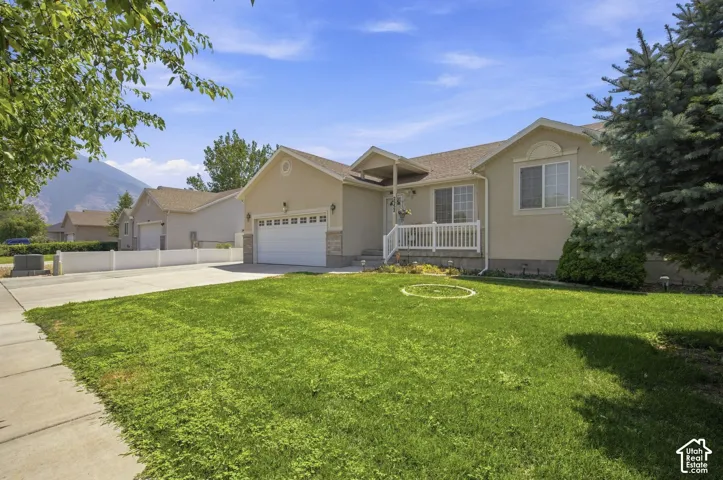 Welcoming single-story residence featuring a tan exterior with covered front porch, two-car garage, and expansive manicured lawn bordered by mature landscaping