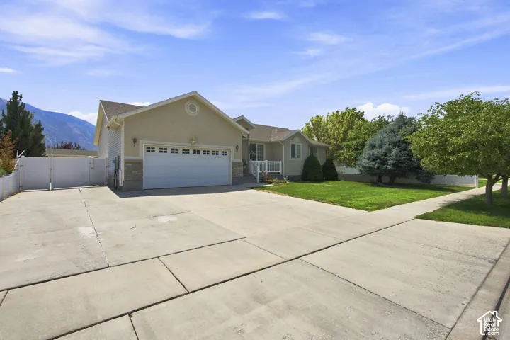 Welcoming front elevation featuring a two-car garage with paneled doors, concrete driveway with clean geometric divisions, neutral exterior siding, pitched roofline with gable detailing, and mature landscaping with established trees framing the property