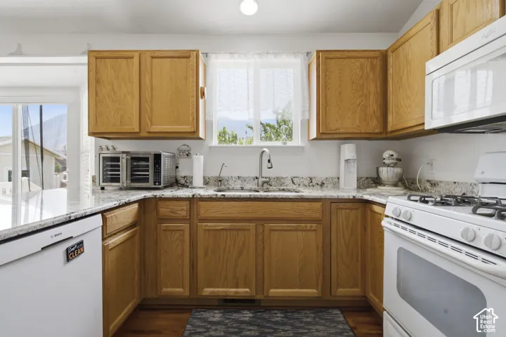 Warm wood cabinetry frames this well-appointed kitchen, featuring granite countertops, appliances including a gas range, and abundant natural light from multiple windows