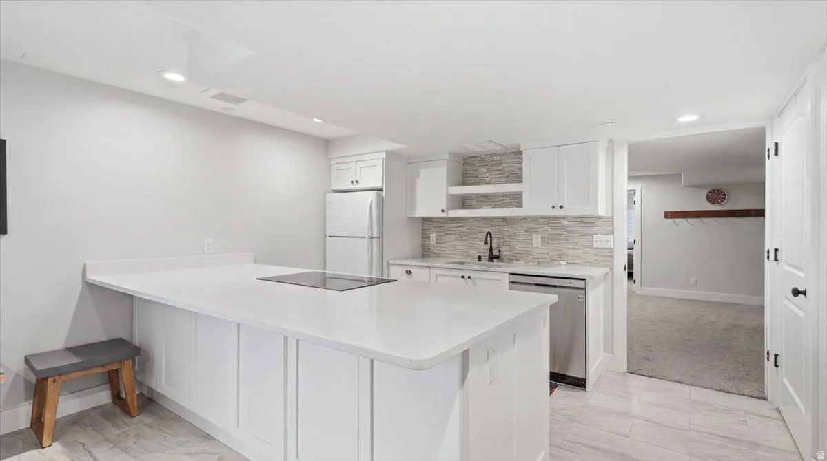 Contemporary kitchen featuring white cabinetry, a built-in cooktop on the island, stainless steel appliances, a tile backsplash, and recessed lighting