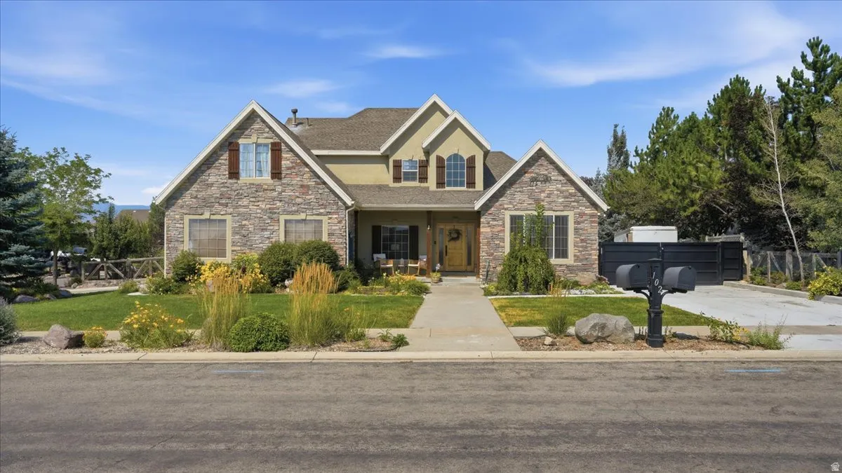 Elegant two-story stone and siding residence featuring a symmetrical facade with multiple gabled rooflines, arched entryway, and professionally landscaped front grounds