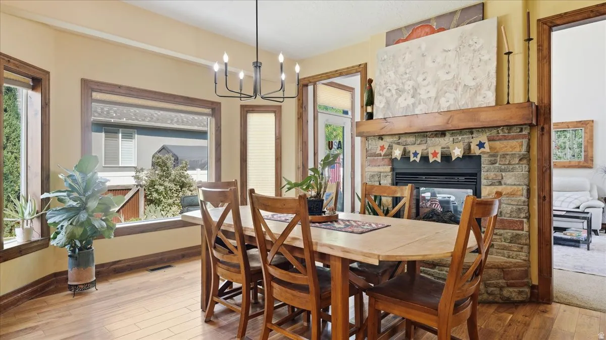 Warm dining room showcasing hardwood flooring, a wood dining table with matching chairs, and a striking brick fireplace with stone surround and mantelpiece