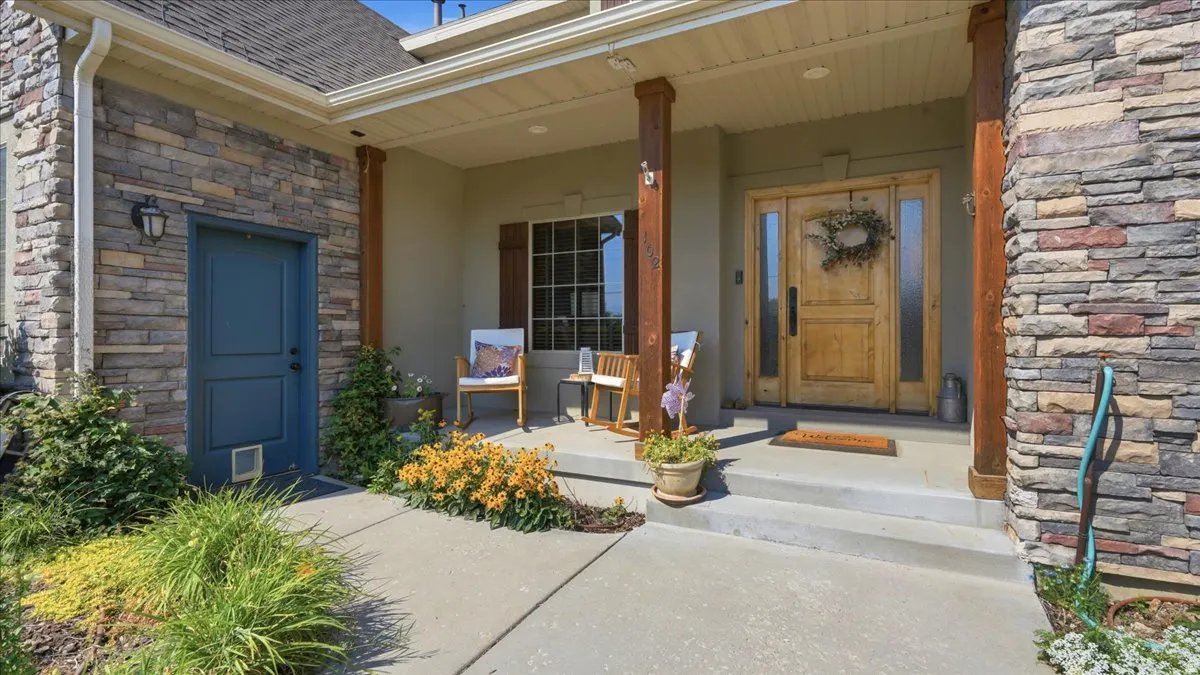 Welcoming front entry featuring a covered porch with wooden support columns, stone and brick exterior, and dual wooden entry doors with sidelights