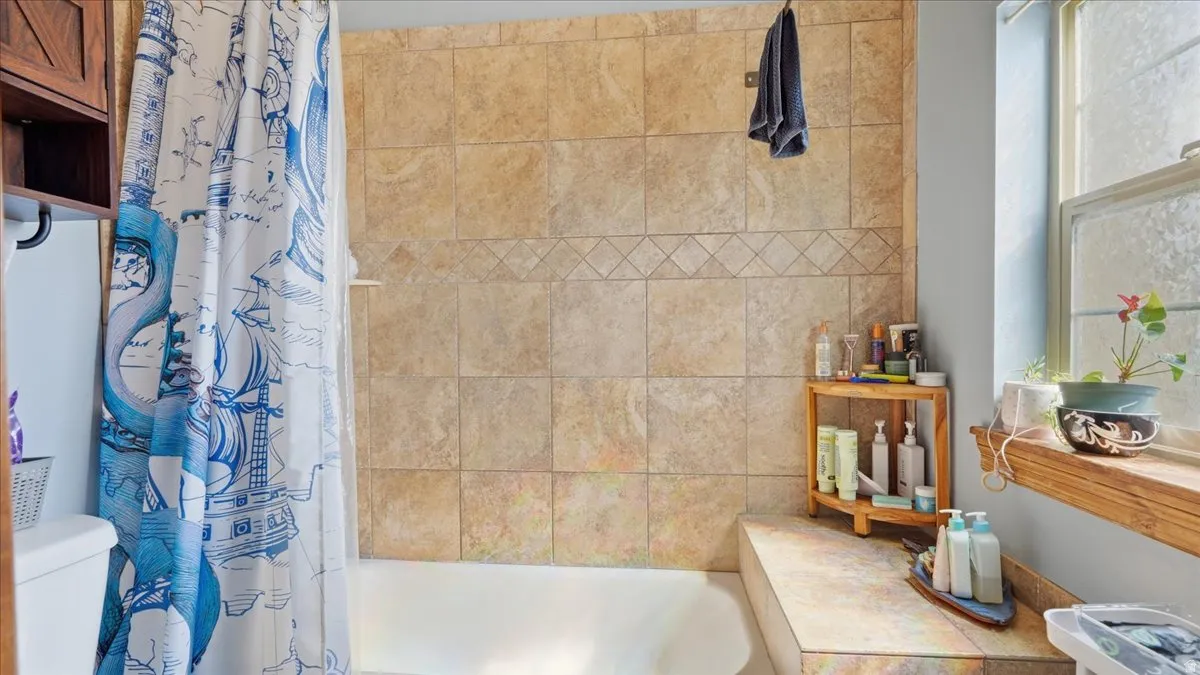 Spa-inspired bathroom featuring a tiled shower surround with warm travertine-look tiles, a soaking tub, and a wood-finish vanity with integrated storage