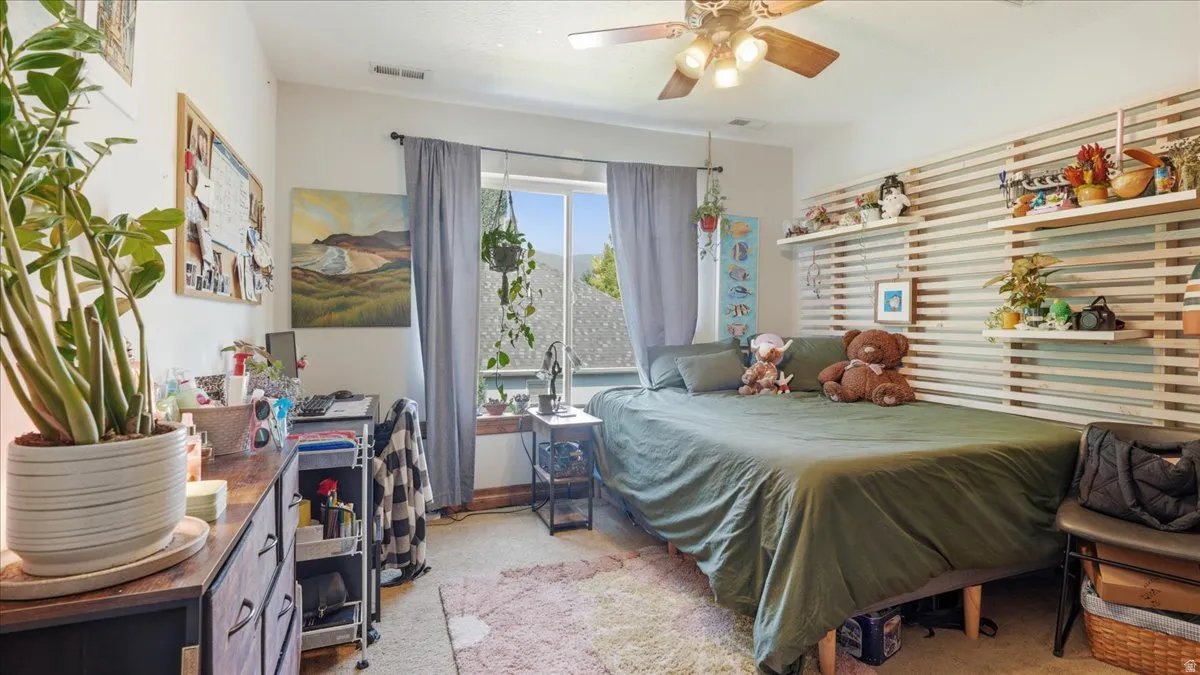 Bright bedroom showcasing abundant natural light through large windows, wood-finish flooring, and a ceiling fan with integrated lighting