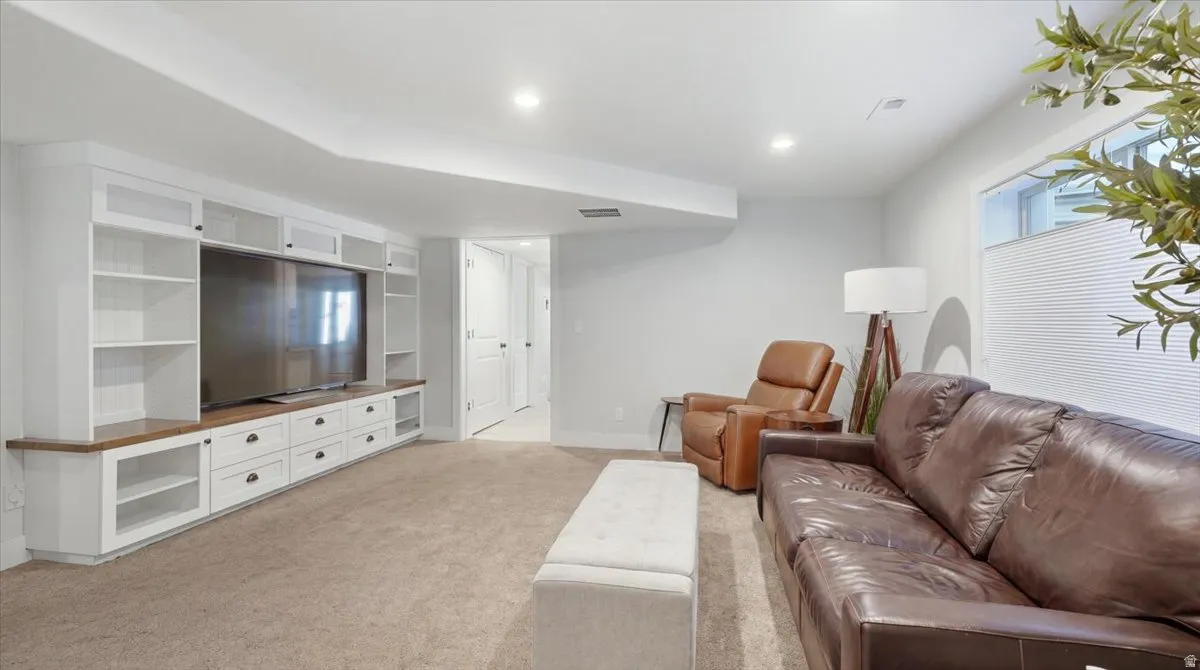 Spacious recreation room featuring custom built-in cabinetry with display shelving, a media center with dark accent paneling, and neutral carpet flooring