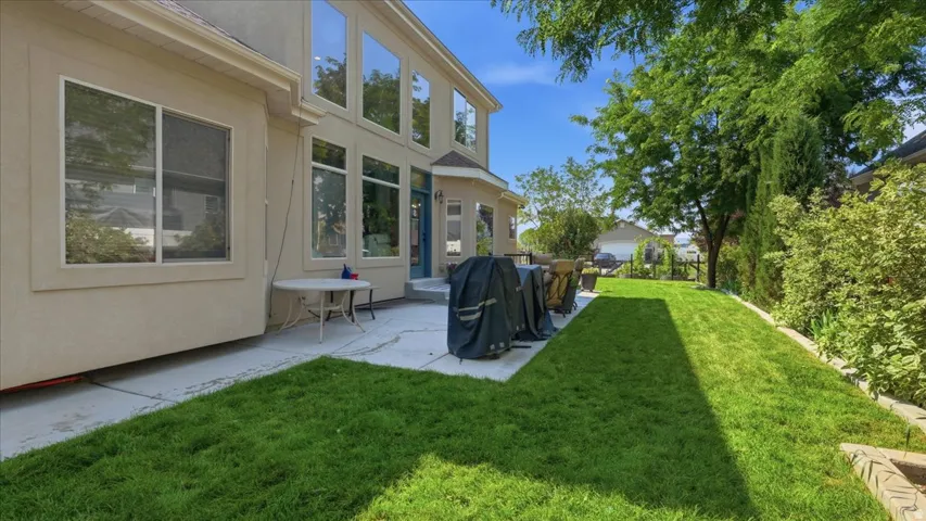 Expansive rear yard featuring a concrete patio, manicured lawn, and mature trees