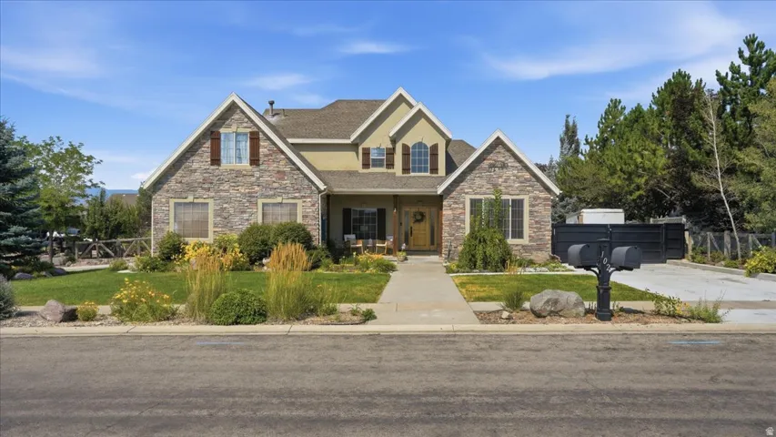 Elegant two-story stone and siding residence featuring a symmetrical facade with multiple gabled rooflines, arched entryway, and professionally landscaped front grounds