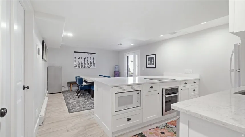 Modern kitchen and open living space featuring white cabinetry with integrated appliances, including dual built-in ovens and a gas cooktop