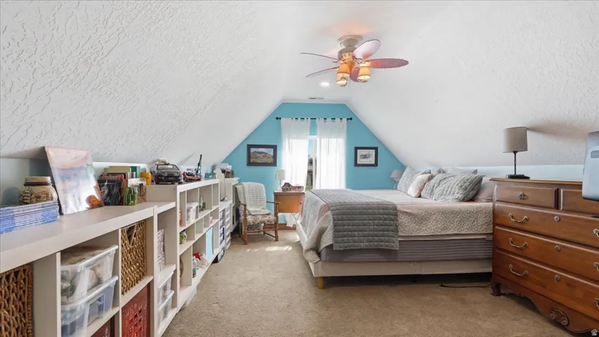 Charming attic bedroom featuring vaulted ceilings with exposed beams, turquoise accent wall paneling, and abundant natural light from dual windows