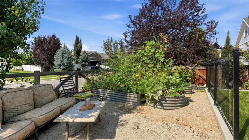 Landscaped outdoor area featuring multiple corrugated metal raised garden beds, a gravel patio surface, and mature perimeter trees