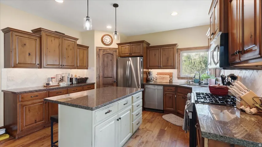 Kitchen featuring wood-finish flooring, rich wood cabinetry, stainless steel appliances, and a central island with a contrasting base and stone countertop