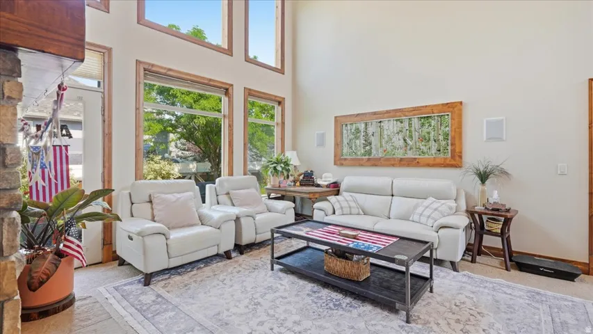 Spacious living area featuring high ceilings, tall windows with wood trim, built-in wall speakers, and a stone-clad fireplace