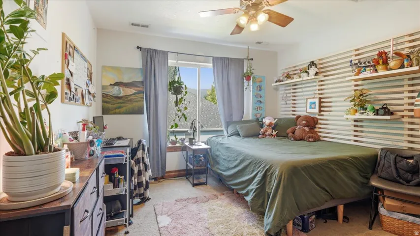 Bright bedroom showcasing abundant natural light through large windows, wood-finish flooring, and a ceiling fan with integrated lighting
