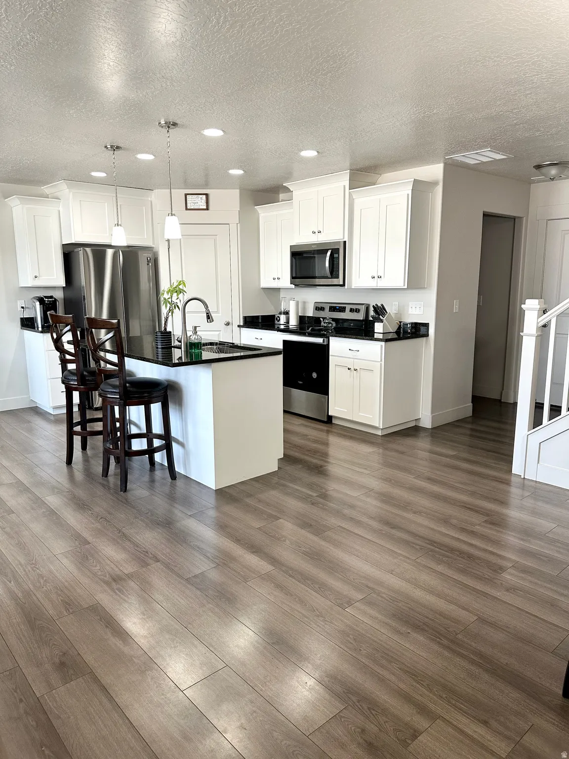 Modern kitchen featuring white shaker cabinetry, stainless steel appliances, dark stone countertops, and wood-finish flooring