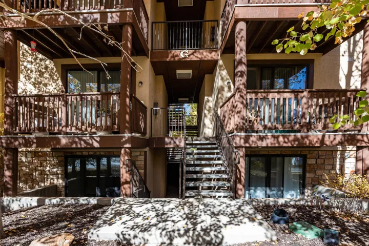 Multi-story exterior featuring wood balconies with balustrades, stucco siding, and stone veneer accents