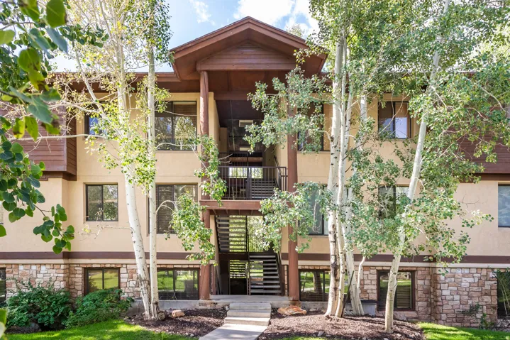 Multi-story residential building featuring a stone veneer base, stucco siding, and dark wood accents