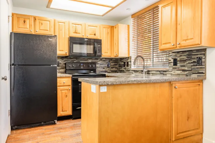 Warm wood cabinetry and granite countertops define this well-appointed kitchen, featuring stainless steel appliances including a black range and microwave, a black refrigerator with freezer, and a single-basin sink with chrome faucet