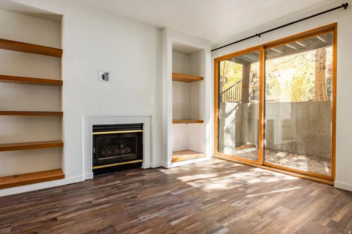 Living area featuring a fireplace with a black and brass insert, custom built-in shelving, wood-finish flooring, and a large sliding glass door with wood framing