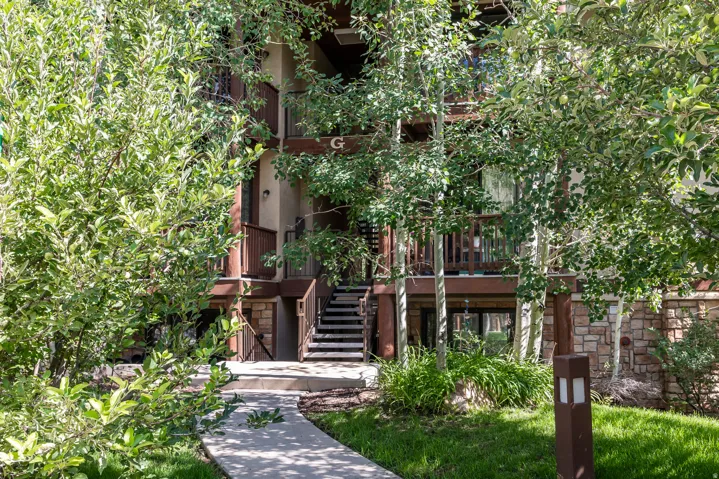 Brick exterior with lush ivy coverage and mature landscaping, featuring a welcoming entry with wooden stairs, multiple levels of architectural detail, and abundant natural greenery throughout the grounds