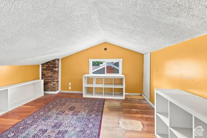 Bright and spacious attic room featuring warm golden-yellow walls, white ceiling with peaked architectural detailing, and hardwood flooring throughout