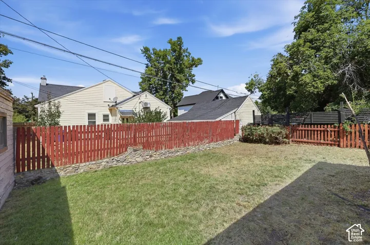 Spacious backyard oasis featuring a manicured lawn, mature shade trees, and sturdy red wood-finish fencing