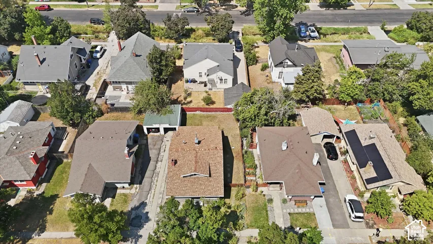Aerial view showcasing a well-appointed residential property featuring a composite or asphalt shingle roof with multiple sections, established mature landscaping throughout the lot, and defined hardscaping elements