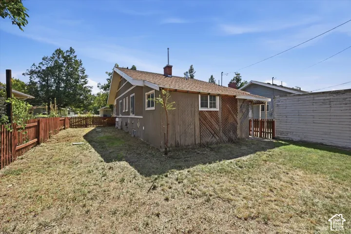 Expansive backyard featuring a brown wooden fence, a small gate, a partial concrete foundation, and an exterior wall with vertical and diagonal wood paneling