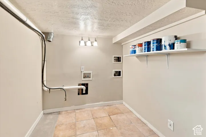 Utility room featuring ceramic tile flooring, white drywall, recessed ceiling with pendant lighting, wall-mounted shelving with storage containers, electrical outlets, and plumbing infrastructure