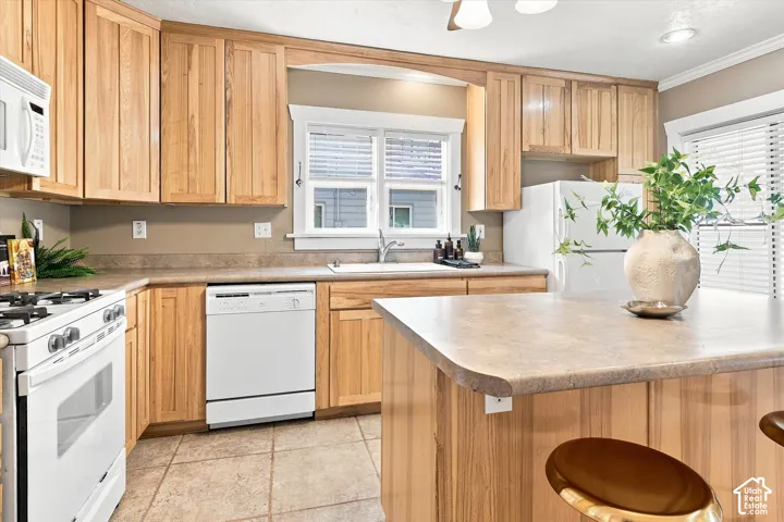 Warm wood cabinetry frames this kitchen featuring white appliances, a tile-finish flooring, neutral countertops, and a center island with seating