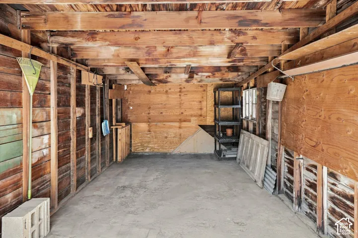 Spacious wooden storage structure featuring exposed beam ceiling, concrete flooring, and built-in wall shelving throughout